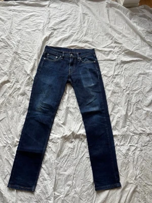 Mörkblå Levi's jeans straight fit - Snygga mörkblå jeans från Levi's med klassisk femficksdesign och raka ben. Jeansen har subtila slitningar framtill och tydliga kontrastsömmar. Perfekta för en avslappnad och stilren look. 30/32