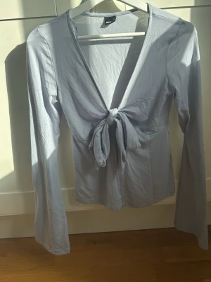 Ljusblå långärmad knytblus  - Trendig ljusblå långärmad blus från gina tricot med djup v-ringning och snygg knytning framtill. Perfekt att styla med jeans eller kjol till sommaren. Mjukt material som känns skönt mot huden.