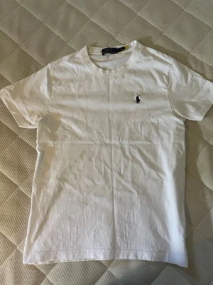 Vit t-shirt från Polo Ralph Lauren - Klassisk vit t-shirt från Polo Ralph Lauren med liten broderad logga på bröstet. T-shirten har rund halsringning och korta ärmar. Tillverkad i mjuk bomull som känns skön mot huden. Perfekt basplagg till garderoben.
