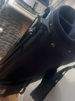 Svart golfbag med axelrem - Säljer en svart golfbag med flera fack och praktisk axelrem. Väskan har robusta detaljer i plast och tygmaterial, perfekt för att organisera golfklubbor. Enkel att bära och smidig att ta med till golfbanan.