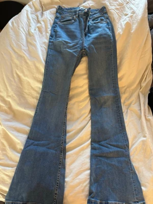 Blå bootcut jeans - Säljer ett par blå bootcut jeans med hög midja och rå kant längst ner. Klassisk femficksmodell i mjukt denimtyg. Perfekta för dig som gillar retrostil och vill ha ett par jeans med lite extra attityd.