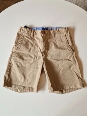 Chinos shorts GANT - Klassiska beiga shorts från GANT i mjuk bomull. De har normal passform, bälteshällor, sidofickor och bakfickor med knapp. Perfekta för varma dagar och enkel att matcha med olika stilar. Använda en gång vid utan några tecken på slitage. Nypris ligger just nu på 480kr!