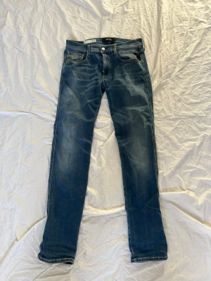 Blå slim fit jeans från Replay - Snygga blå slim fit jeans från Replay med klassisk femficksdesign och diskreta slitningar. Jeansen har normal midja, dragkedjegylf och silverfärgade detaljer. Perfekta för en trendig och avslappnad look.