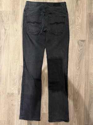 Nudie Jeans Slim Jim Jeans Mörkgrå W31/L34 - Slim Fit - Nudie Slim Jim mörkgrå jeans i stretchig denim med slim fit passform som sitter snyggt och bekvämt och funkar till allt, storlek W31/L34, midja 37 cm, ytterbenslängd 107 cm, benöppning 18,5 cm, modellen är 185cm & väger 65kg, i fint skick.