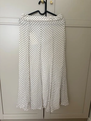 Polkadot midikjol från Zara  - Supersnygg långkjol från NA-KD i vit med svarta prickar. Kjolen har en flowy passform och är tillverkad i ett lätt och mjukt material som känns skönt mot huden. Perfekt att styla med en enkel topp och sneakers för en trendig look.