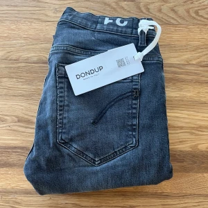 Dondup George Jeans - Snygga svarta jeans från Dondup med klassisk femficksdesign och raka ben. Jeansen har en mörk tvätt med lätt slitning och är tillverkade i mjukt bomullsmaterial med stretch för extra komfort. Perfekta för dig som gillar en stilren look. Storlek W31 | Ny pris=3000kr | Mitt pris, endast 549!!