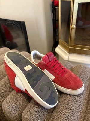Valentino Flycrew - Snygga röda sneakers från Valentino med ovandel i rött mocka och vita detaljer på sidan. Skorna har vita sulor med unikt mönster undertill och röda skosnören. Låg modell som passar perfekt till streetwear och casual outfits. Skick 7,5/10 (2 nitar saknas, lite sliten häl, lite stygn som släppt) pris ej hugget i sten.
