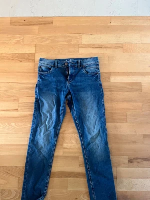 Blå slim fit jeans med fem fickor - Snygga blå slim fit jeans med klassisk femficksdesign och normalhög midja. Jeansen har slitningar och ljusare partier framtill för en trendig look. Passar perfekt till en avslappnad stil och är lätta att matcha med olika toppar. Från Kappahl