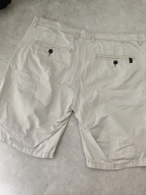 Beige shorts från H&M - Snygga beige shorts från H&M med klassisk passform. Shortsen har två sidofickor fram och två bakfickor med knapp. Perfekta för varma dagar och enkla att matcha med olika stilar.