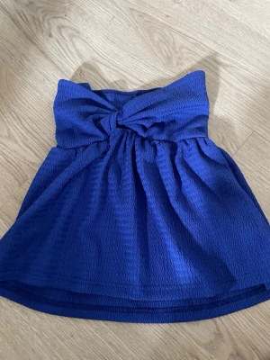Blå bandeau topp från SHEIN - Säljer en blå bandeau topp från SHEIN med twistad detalj framtill. Toppen är axelbandslös och har en lätt strukturerad yta i syntetmaterial. Perfekt för dig som vill ha en enkel men snygg topp till sommaren.ej använd 