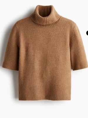 Beige stickad polotröja med kort ärm - Stickad beige polotröja med korta ärmar och bred ribbad kant vid hals, ärmslut och nederkant. Tröjan har en avslappnad passform och är perfekt för lager-på-lager. Enkel och stilren design som passar till mycket.