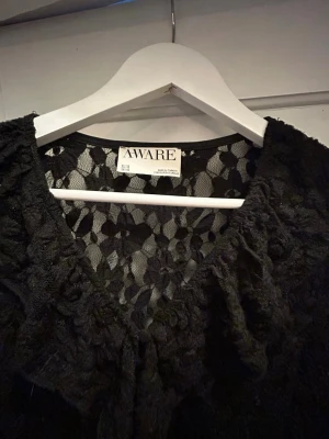 Svart spetsblus med volang från Aware - Snygg svart blus från Aware i transparent spets med volangdetaljer längs ringningen och framtill. Köpt på Bik Bok 