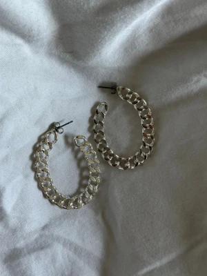 Silvriga chunky kedjeörhängen - Snygga örhängen i form av stora hoops med kedjelänk-design i silverfärgad metall. De har en chunky och trendig look som passar perfekt till en cool streetstyle. Märke saknas.