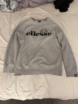 Grå sweatshirt från Ellesse - Snygg grå sweatshirt från Ellesse med svart logga tryckt på bröstet. Den ända defekten jag kan hitta är en liten fläck på framsidan men ingen märkbart och de går förmodligen bort med exempelvis vanish. 