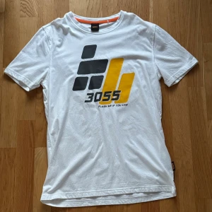 Boss T-shirt - BOSS T-shirt i vit färg med stort tryck framtill, med en lite futuristisk/sci-fi känsla. Sportig och lättmatchad modell, perfekt till vardags eller casual outfits.