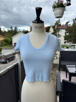Ljusblå croppad topp med v-ringning - Söt ljusblå croppad topp med v-ringning och korta ärmar. Toppen har vågig kant nertill och är gjord i ett mjukt, stretchigt material som sitter tajt 💙