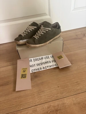 Olivgröna Golden Goose sneakers - Snygga olivgröna sneakers från Golden Goose med ovandel i mocka och vita skosnören. Skorna har en låg silhuett och svart detalj på hälen. Perfekta för dig som gillar en stilren och trendig look. Skorna är i storleken 43 och är varsamt använda. Tveka inte på att skriva vid minsta lilla fundering. Pris kan gå ner vid snabb affär⚜️🔥🙌