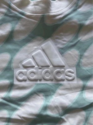 Adidas/Marimekko träningstopp / kroppad topp - M - Super snygg Adidas/Marimekko träningstopp / kroppad topp. DETAILS • Loose fit • Ribbed crewneck • 93% cotton, 7% elastane single jersey • Crop length Köpt på stadium Storlek Medium