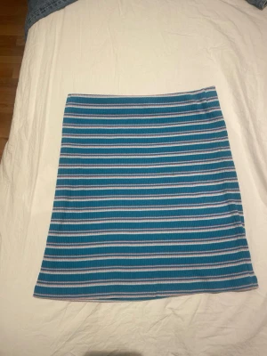 Randig blå och vit ribbad kortkjol - Säljer en söt ribbad kortkjol med blå och vita ränder. Kjolen har en rak passform och är perfekt för dig som gillar en enkel men stilren look. Materialet är mjukt och stretchigt vilket gör den bekväm att bära hela dagen.