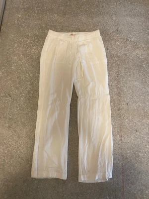 Vita linnebyxor från Nelly  - LOW WAIST! Snygga vita linnebyxor med raka ben och klassisk passform. Byxorna har fickor fram och ett diskret band i midjan för extra komfort. Perfekta för en avslappnad och stilren look under varma dagar.