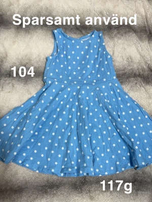Blå prickig klänning barn - Söt blå klänning med vita prickar och ärmlös design. Klänningen har rund halsringning och utställd kjol, perfekt för en lekfull stil. Lätt och bekväm att bära, passar bra till varma dagar.🌸 Sparsamt använd. Storlek 104