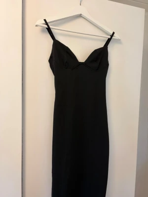 Svart långklänning från Missguided - Elegant svart långklänning från Missguided med smala axelband och figurnära passform. Klänningen har en djup urringning och är tillverkad i ett mjukt, stretchigt material som ger en snygg siluett.