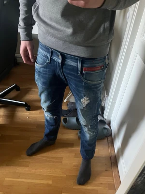 Replay jeans - Säljer ett par blå jeans från Replay med snygga slitningar och distressed detaljer. Nästan helt nyskick.  De är storlek 30/32 men de passar mindre.  Innerbenslängd är 68 cm och midjemått är 78 cm. Hör gärna av dig vid frågor!
