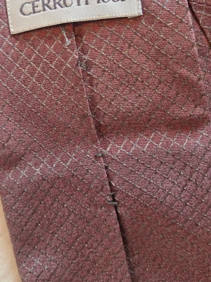 Rutig slips från Cerruti 1881 - Säljer en elegant slips från Cerruti 1881 i vinröd nyans med diskret rutigt mönster. Slipsen har en klassisk form och är tillverkad i ett glansigt material som ger en lyxig känsla. Perfekt för att lyfta din outfit med en stilren detalj.