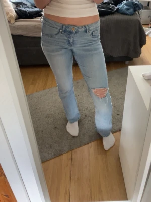 Ljusblå jeans  - Säljer ett par ljusblå jeans med lite utsvävning vid bena och snygga slitningar på ena låret. Jeansen har klassisk femficksdesign och normal midja. Perfekta för en avslappnad och trendig look. (De vita märkerna på sista bilden är inget som blivit när jag har använt de, utan de var där när jag köpte jeansen)