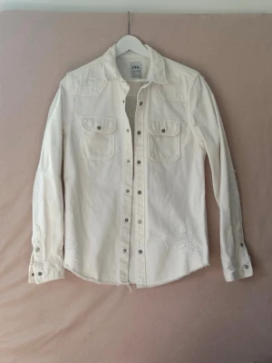 Vit jeansjacka från ZARA - Vit jeansjacka/overshirt i S ( S-XS ?) från Zara. Tyget är lite av det hårda materialet dvs. inte stretch. Klassisk krage och diskreta slitningar för en trendig look.  Se ca-mått i cm: Axel: 42-43 Bröst: ca 48 Längd: ca 72 Ärmar: ca 51 ( mätt från armhålan). I nyskick. 
