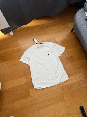 Vit t-shirt från Ralph Lauren - Vit t-shirt från Ralph Lauren med klassisk passform och liten broderad logga på bröstet. T-shirten har rund halsringning och är tillverkad i mjuk bomull, perfekt för en clean och stilren look. Obs❗️ i helt ny skick köptes på Plick men var tyvärr förstor för mig därmed säljer jag denna fina T- shirt 