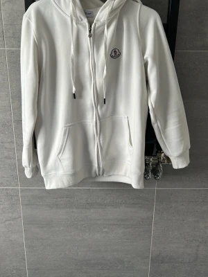 Vit zip hoodie från Moncler - Snygg vit hoodie från Moncler med dragkedja, huva på baksidan. Den är skön i materialet men säljer den pga att den är för liten för mig. Storleken är Small 