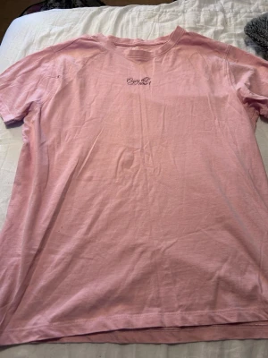 Rosa t-shirt från 157 med tryck - Ljusrosa t-shirt från 157 med texten 'Enjoy the now!' tryckt på bröstet. Klassisk rund halsringning och korta ärmar. Tillverkad i mjuk bomull som känns skön mot huden. Perfekt för en avslappnad och trendig look.