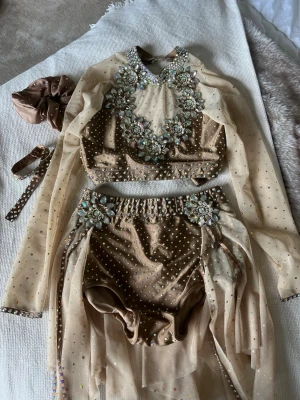 Glittrig beige slowdräkt - Gullig slowdräkt med mycket detaljer och strass! Fotband och toffs följer med! Passar en xs! Är i bra skick och glittrar väldigt fint på golvet