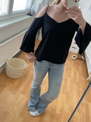 Svart offshoulder topp med vida ärmar - Snygg svart offshoulder topp med vida, utsvängda ärmar och smala axelband. Toppen har en v-ringad. Materialet känns lätt och luftigt.