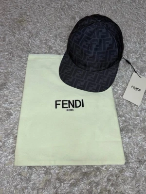 Svart keps med Fendi-logga - Snygg svart keps från Fendi med klassiskt FF-monogram över hela kepsen. Justerbar baktill och tillverkad i ett slitstarkt tyg. Perfekt accessoar för att lyfta din streetwear-look.