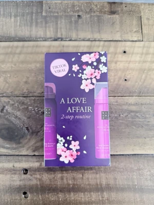 Rituals A Love Affair 2-step kit - Säljer ett Rituals A Love Affair 2-step routine kit med duschskum och body lotion. Förpackningen är lila med blommiga detaljer och innehåller två produkter i smidigt format. Perfekt för dig som vill testa en populär hudvårdsrutin.