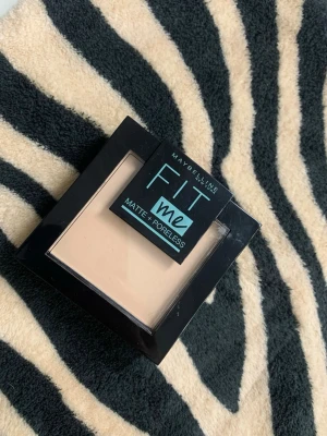 Maybelline Fit Me Matte + Poreless puder - Maybelline Fit Me Matte + Poreless foundationpuder i en ljus beige nyans. Kommer i en fyrkantig svart plastförpackning med genomskinligt lock. Perfekt för en matt finish och jämn hudton.