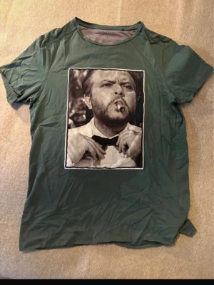 Limitato tröja - Stilren grön t-shirt från LIMITATO med ett stort svartvitt tryck av en man som röker cigarr på bröstet. T-shirten har rund hals och korta ärmar, perfekt för en avslappnad look.