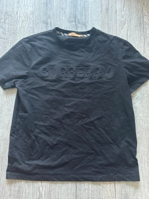 Svart Burberry t-shirt i bomull - Snygg svart t-shirt från Burberry med stort, upphöjt Burberry-tryck på bröstet. Klassisk rund halsringning och korta ärmar. Tillverkad i mjuk bomull för en skön känsla och stilren look.