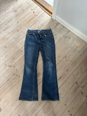 Blå bootcut jeans med slitningar - Säljer ett par blå bootcut jeans med lätt slitna detaljer och klassisk femficksmodell. Jeansen har en något utsvängd passform nedtill och är tillverkade i denim. Perfekta för dig som gillar en retroinspirerad look. Jeansen är bootcut. Skriv för fler bilder 😊
