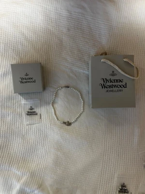 Vivienne Westwood pärlhalsband - Snyggt halsband från Vivienne Westwood med vita pärlor och det ikoniska orb-hänget i silverfärg med gnistrande stenar. Kommer med originalask och påse. Perfekt accessoar för dig som vill sticka ut med en klassisk men edgy stil.