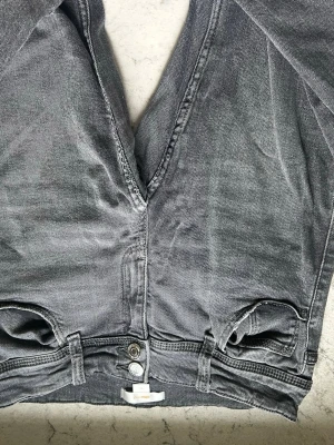 Grå jeans från Gina Tricot - Säljer ett par grå jeans från Gina Tricot med snygg tvättad look och dubbla silverknappar i midjan. Klassisk femficksmodell med bälteshällor och flare ben. Materialet är slitstark denim i bomull. Perfekta för en avslappnad och trendig stil. Har sytt upp dem lite, pågrund av att dem va för långa.