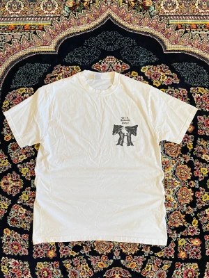 Vit t-shirt från Russell med tryck - Säljer en vit t-shirt från Russell i storlek M. T-shirten har ett svart tryck på bröstet med texten 'GET A GRIP ON GRIPS' och illustration. Klassisk rund hals och korta ärmar. Tillverkad i mjuk bomull, perfekt för en clean och enkel stil.