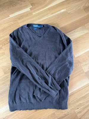 Brun V-ringad tröja Polo Ralph Lauren - Mjuk brun stickad tröja från Polo Ralph Lauren i 100% pima bomull. Klassisk V-ringning och diskret broderad logga på bröstet. Långa ärmar och ribbade muddar vid ärmslut och nederkant. Perfekt för en stilren och avslappnad look. Pris kan diskuteras vid snabb köp