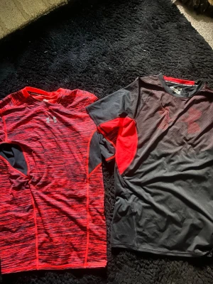 Två Under Armour tränings-tshirts - Kan böja mig i priset skicka medelande vid frågor. Säljer två snygga tränings-tshirts från Under Armour. Ena är röd med svarta detaljer och mönster, den andra är svart med röda inslag och mesh-tyg framtill. Båda har kort ärm och är tillverkade i funktionsmaterial som andas, perfekta för gym eller löpning.