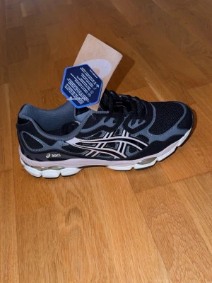 Svarta Asics sneakers med meshdetaljer - Snygga svarta sneakers från Asics med vita och grå detaljer. Skon har en sportig design med meshpaneler för bra ventilation och en rejäl, stötdämpande sula. Perfekt för dig som gillar streetwear och bekväma skor med stil.