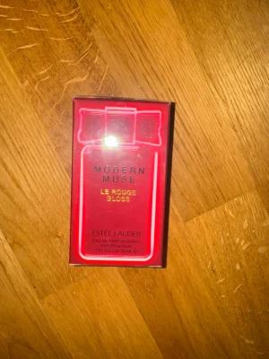 Modern Muse Le Rouge Gloss parfym - Modern Muse Le Rouge Gloss från Estée Lauder är en Eau de Parfum i en snygg röd förpackning med gulddetaljer och motiv av en parfymflaska med rosett. Innehåller 30 ml och har en lyxig och modern design.