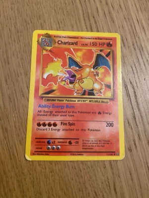 Charizard Pokémonkort 2016 - Säljer ett Charizard Pokémonkort från 2016 med gul ram och klassisk design. Kortet har motiv av Charizard med eld och detaljer i rött, orange och blått. Perfekt för samlare eller Pokémonfans som vill utöka sin kortsamling.