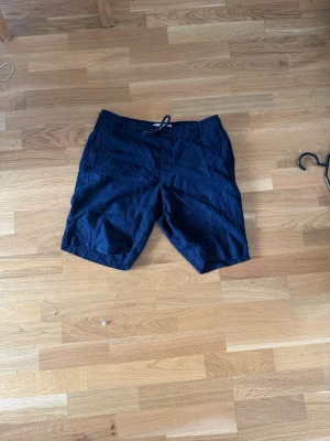 Mörkblå linneshorts från Dressmann - Säljer ett par mörkblå shorts från Dressmann i linnemix. Shortsen har snörning i midjan och avslappnad passform, perfekta för varma dagar. Klassisk design utan mönster och med fickor på sidorna.